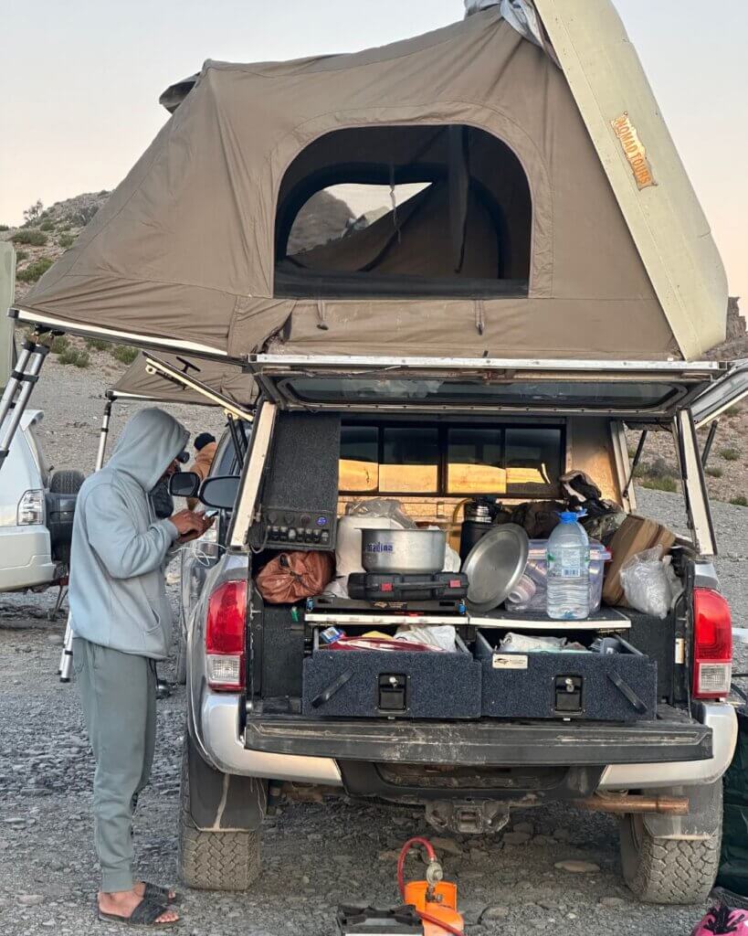 Camping and cooking equipment set up next to a rental car during an Oman road trip.