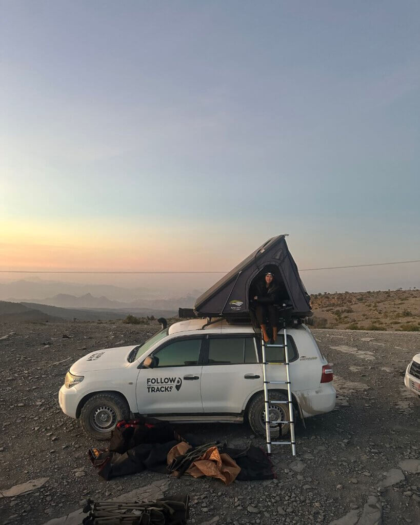 Camping and cooking equipment set up next to a rental car during an Oman road trip.