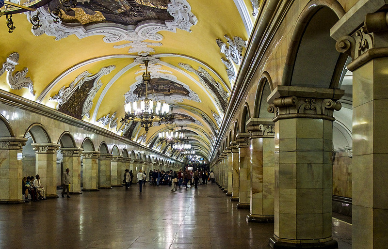 Panoramic view of Komsomolskaya metro station in Moscow, highlighting its vast hall with chandeliers and decorative mosaics.